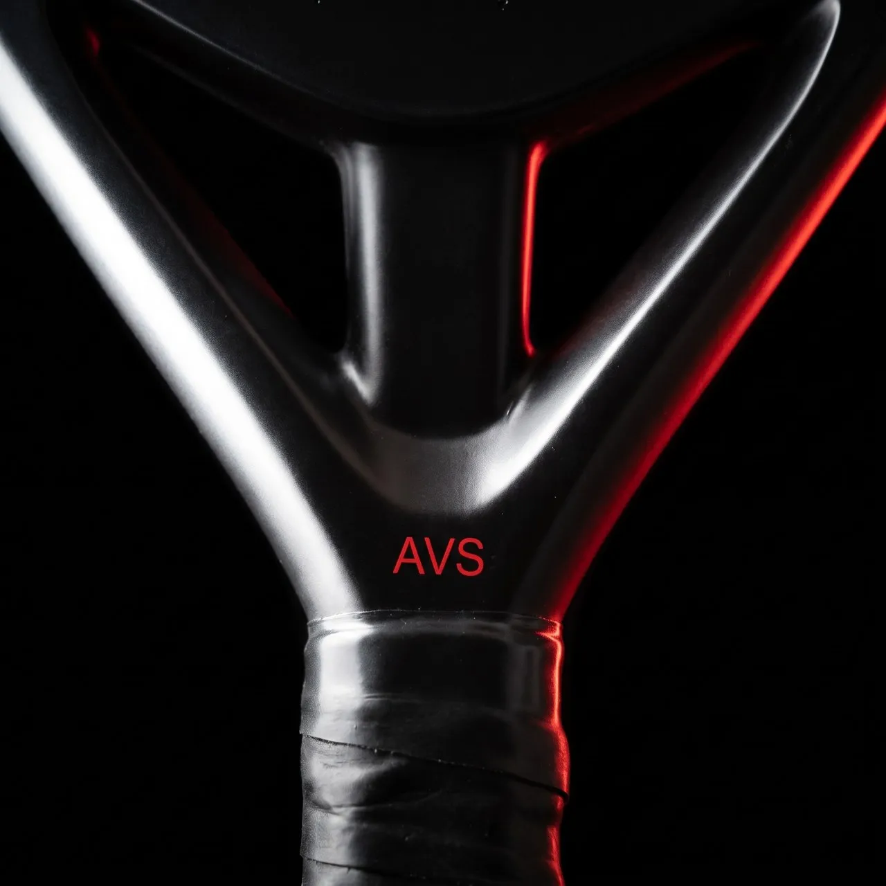 Macro du cœur d'une raquette SCUD Black Impact B3 : la fourche gunmetal, la marque AVS rouge à sa base et les premiers tours du grip